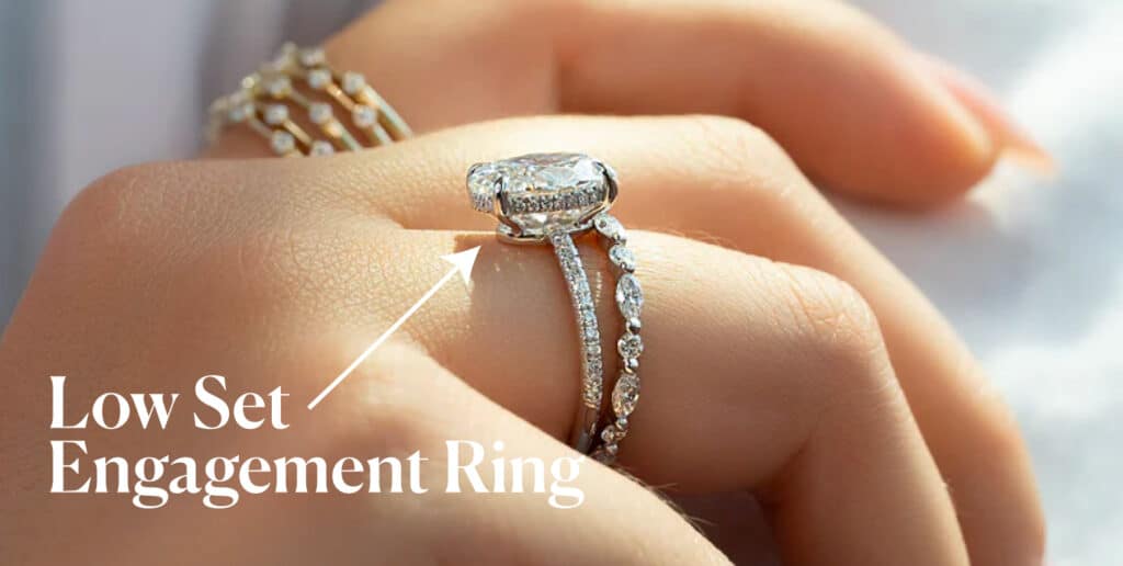 A close-up view of a hand wearing a low-set engagement ring paired with a diamond-studded band. The ring features a diamond that sits low and close to the finger, offering a practical and elegant design.