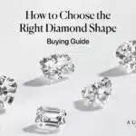 A featured image for an expert buying guide titled "How to Choose the Right Diamond Shape." The image displays five different, high-quality loose diamonds artfully scattered as if they are floating against a clean, bright, neutral background. The featured diamond shapes include some of the most popular and distinct styles: a large Oval cut, a Cushion cut, a Heart shape, a sophisticated Emerald cut, and what appears to be a brilliant Radiant cut. This professional, high-end photograph is designed to instantly showcase the beautiful variety of shapes available, drawing the reader into the comprehensive buying guide. The Aurelia brand logo is subtly placed in the corner.