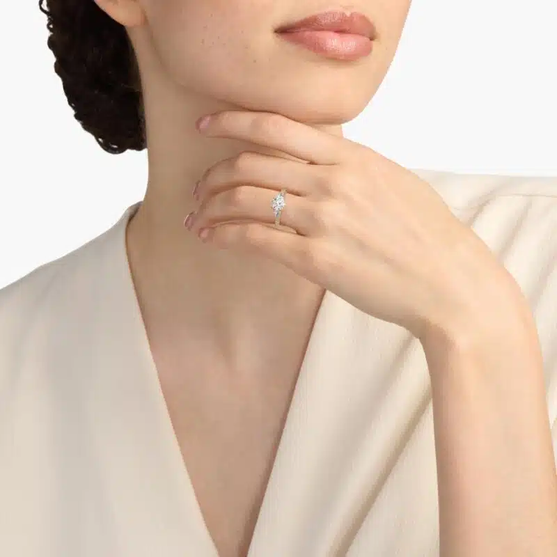 A woman's hand wearing a GIA 2.01 carat round diamond engagement ring, showcasing the beautiful three-stone and lace bridge details in 14K yellow gold.