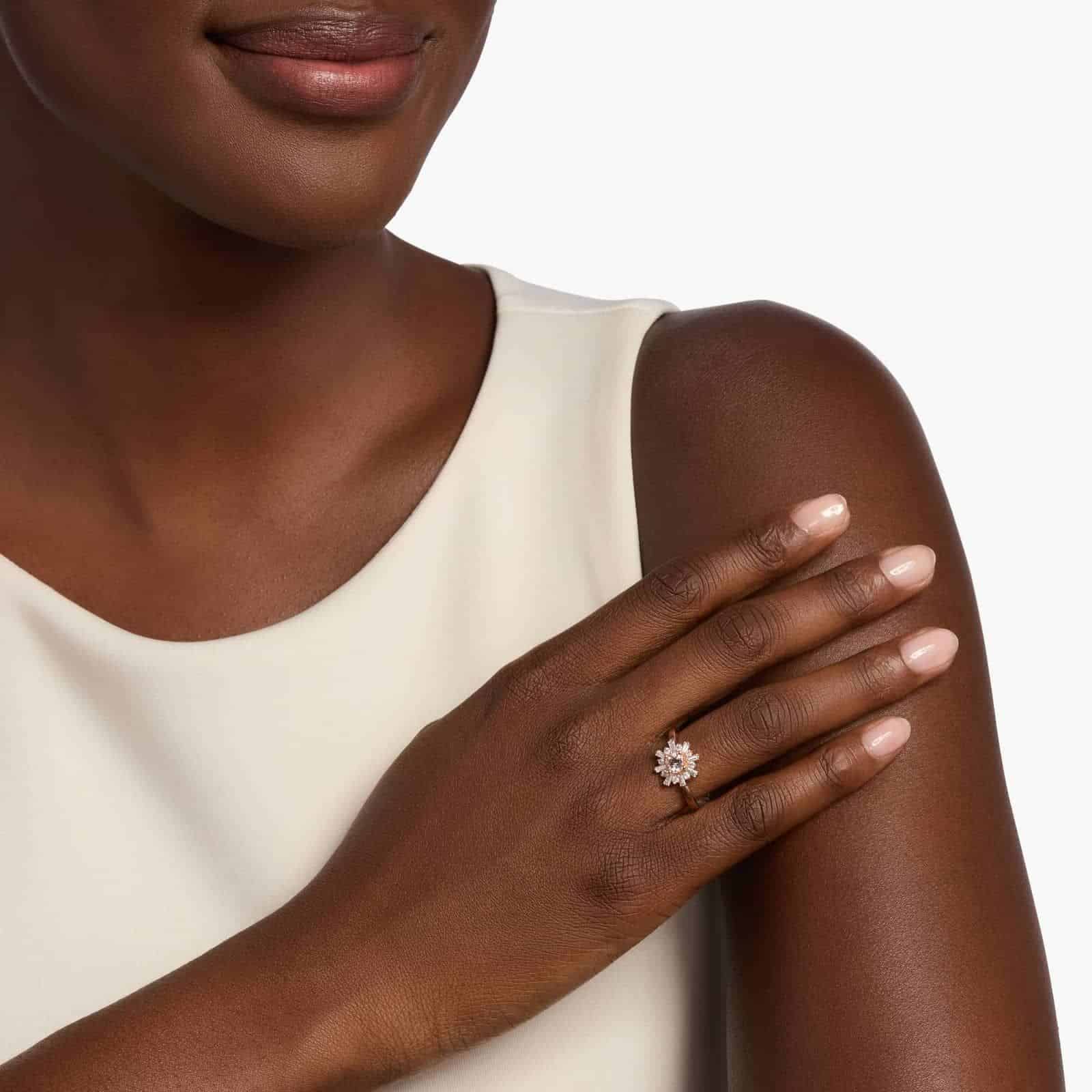 A woman's hand wearing a **Morganite Engagement Ring**, showcasing the round morganite and the unique halo of baguette and round diamonds in 14K rose gold.