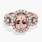 A close-up studio shot of an **oval morganite and diamond ring** on a white background, highlighting the central stone, the bezel-set diamonds, and the intricate pavé detail on the band.