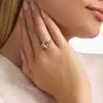 A woman's hand wearing an **Oval Morganite Engagement Ring**, showcasing the brilliant oval morganite and the sparkling pavé diamond band in 14K rose gold.