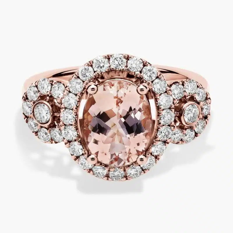 A close-up studio shot of an **oval morganite and diamond ring** on a white background, highlighting the central stone, the bezel-set diamonds, and the intricate pavé detail on the band.