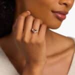 A woman's hand wearing a stunning **oval morganite engagement ring** with diamond sidestones, set in a 14K rose gold band.