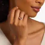 A woman's hand wearing a stunning **oval morganite engagement ring** with diamond sidestones, set in a 14K rose gold band.