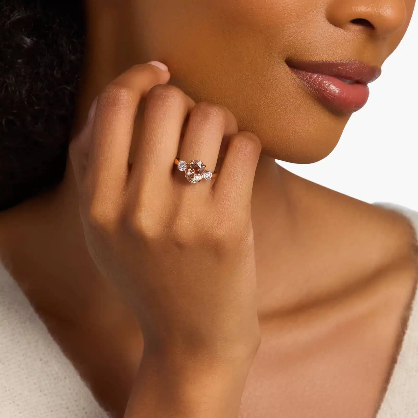 A woman's hand wearing a stunning **oval morganite engagement ring** with diamond sidestones, set in a 14K rose gold band.