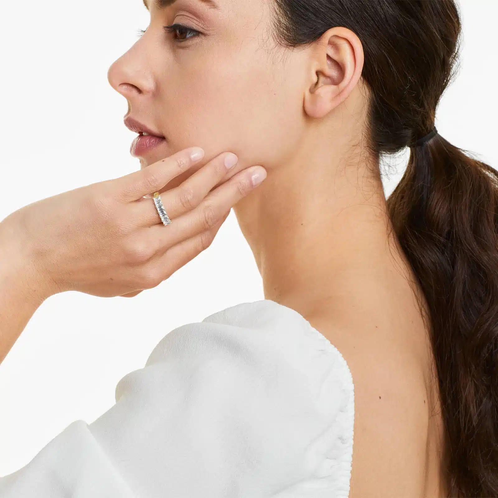 A model wearing the 2 ctw seven stone emerald cut anniversary ring in 14k yellow gold, stacked next to a solitaire engagement ring to show its versatility and scale on a hand.