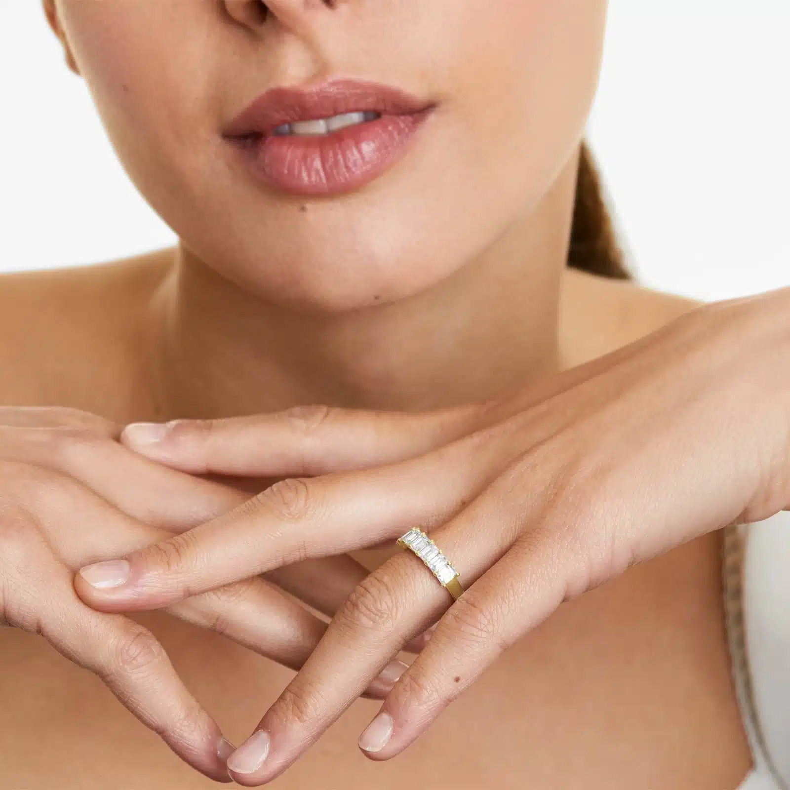 A model wearing the 2 ctw seven stone emerald cut anniversary ring in 14k yellow gold, stacked next to a solitaire engagement ring to show its versatility and scale on a hand.