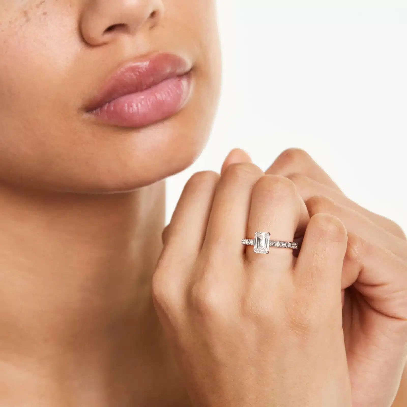 A woman's hand wearing a majestic **7 carat diamond ring**, showcasing the large emerald cut diamond and the sparkling French cut pavé band in platinum