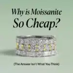 An elegant image showing three stacked rings with glittering moissanite gems on a pale green background. The top ring is a simple band of round stones, the middle ring alternates between round stones and yellow-gold sections, and the bottom ring features baguette-cut stones. The title "Why is Moissanite So Cheap?" is centered above the rings with the subtitle "(The Answer Isn't What You Think)" below them.
