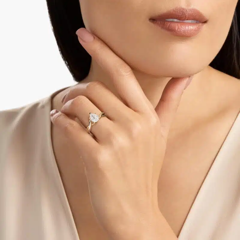 A woman's hand wearing a majestic 7 carat diamond ring, showcasing the large pear-shaped diamond in a twisted solitaire setting in 18k yellow gold.