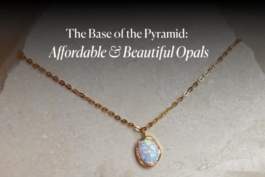 A gold chain necklace with a beautiful, affordable white opal pendant on a light stone surface. The image is titled 'The Base of the Pyramid: Affordable & Beautiful Opals'.