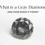 Featured image for the ultimate guide to gray diamonds. A close-up shot of a dark, round brilliant cut gray diamond, titled "What is a Gray Diamond and How Does it Form?". The image showcases the stone's sophisticated, moody gray body color.