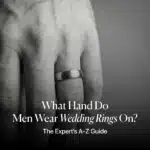 Close-up of a man's hand wearing a brushed metal wedding band on the left ring finger, with the article title overlay: "What Hand Do Men Wear Wedding Rings On? The Expert’s A-Z Guide."