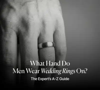 Close-up of a man's hand wearing a brushed metal wedding band on the left ring finger, with the article title overlay: "What Hand Do Men Wear Wedding Rings On? The Expert’s A-Z Guide."