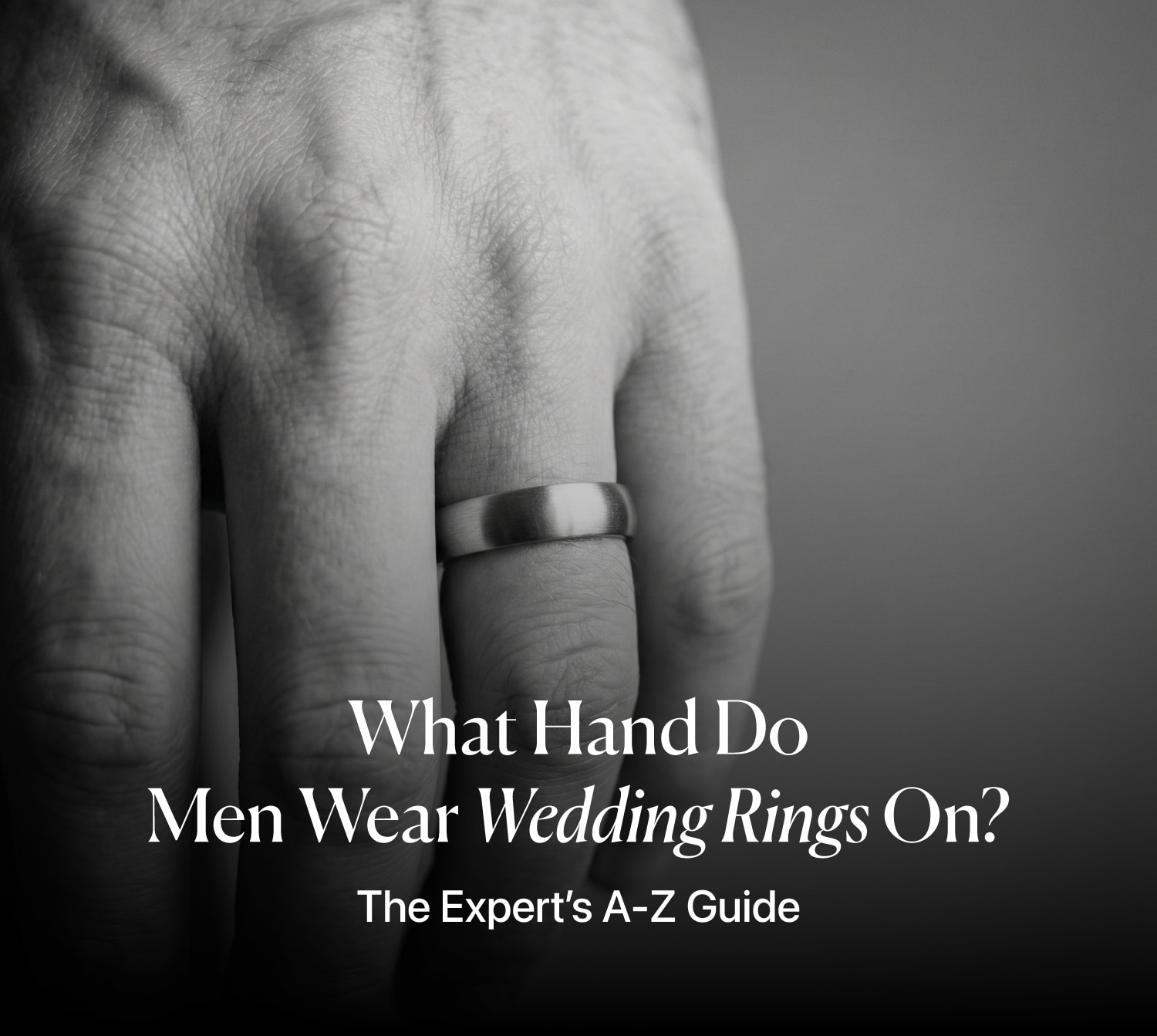 Close-up of a man's hand wearing a brushed metal wedding band on the left ring finger, with the article title overlay: "What Hand Do Men Wear Wedding Rings On? The Expert’s A-Z Guide."