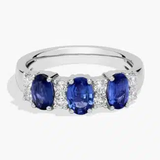 A 14K White Gold 3 Stone Diamond Rings With Sapphires ring (3.60 mm wide) featuring three Oval Blue Sapphires set in prongs, accented by 0.31 CTW Round Diamonds on the shank.