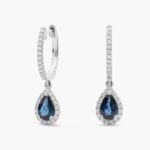 A pair of 14K White Gold Sapphire and Diamond Dangle Earrings featuring two 6x4 mm Pear Shaped Blue Sapphires (1 CT total) and a 0.22 CTW Round Diamond Halo, secured with Hinged Snap Backs.