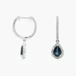 A pair of 14K White Gold Sapphire and Diamond Dangle Earrings featuring two 6x4 mm Pear Shaped Blue Sapphires (1 CT total) and a 0.22 CTW Round Diamond Halo, secured with Hinged Snap Backs.