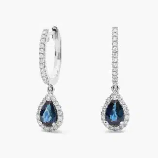 A pair of 14K White Gold Sapphire and Diamond Dangle Earrings featuring two 6x4 mm Pear Shaped Blue Sapphires (1 CT total) and a 0.22 CTW Round Diamond Halo, secured with Hinged Snap Backs.