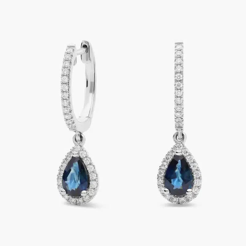 A pair of 14K White Gold Sapphire and Diamond Dangle Earrings featuring two 6x4 mm Pear Shaped Blue Sapphires (1 CT total) and a 0.22 CTW Round Diamond Halo, secured with Hinged Snap Backs.