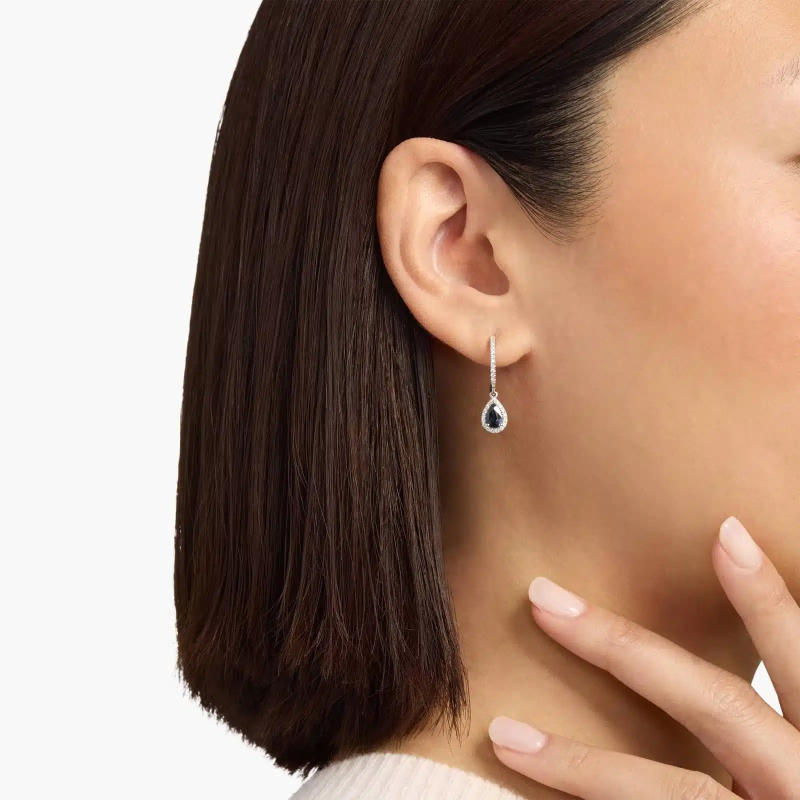 A pair of 14K White Gold Sapphire and Diamond Dangle Earrings featuring two 6x4 mm Pear Shaped Blue Sapphires (1 CT total) and a 0.22 CTW Round Diamond Halo, secured with Hinged Snap Backs.