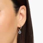 A pair of 14K White Gold Sapphire and Diamond Dangle Earrings featuring two 6x4 mm Pear Shaped Blue Sapphires (1 CT total) and a 0.22 CTW Round Diamond Halo, secured with Hinged Snap Backs.