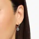 A pair of 14K White Gold Sapphire and Diamond Dangle Earrings featuring two 6x4 mm Pear Shaped Blue Sapphires (1 CT total) and a 0.22 CTW Round Diamond Halo, secured with Hinged Snap Backs.