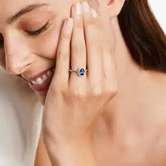 An 18K White Gold Oval Halo Engagement Rings With Diamonds and Sapphires ring featuring a 1.05 Carat Oval Blue Sapphire center stone and a 0.27 Carat Total Weight round diamond halo.