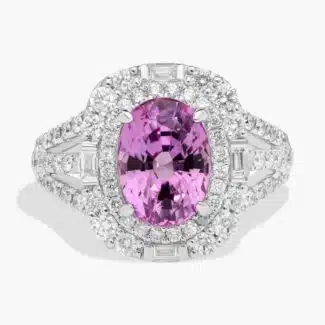 An 18K White Gold Pink Sapphire and Diamond Ring, designed as a Cocktail Ring, featuring a 5.04 Carat Oval Pink Sapphire center stone surrounded by a halo of Round and Baguette diamonds (0.94 CTW total).