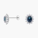 An 18K White Gold White Gold and Sapphire Earrings set featuring two 7x5 mm Oval Blue Sapphires surrounded by a 0.72 CTW Round Diamond Halo, secured with Push Backs.