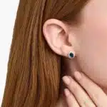 An 18K White Gold White Gold and Sapphire Earrings set featuring two 7x5 mm Oval Blue Sapphires surrounded by a 0.72 CTW Round Diamond Halo, secured with Push Backs.