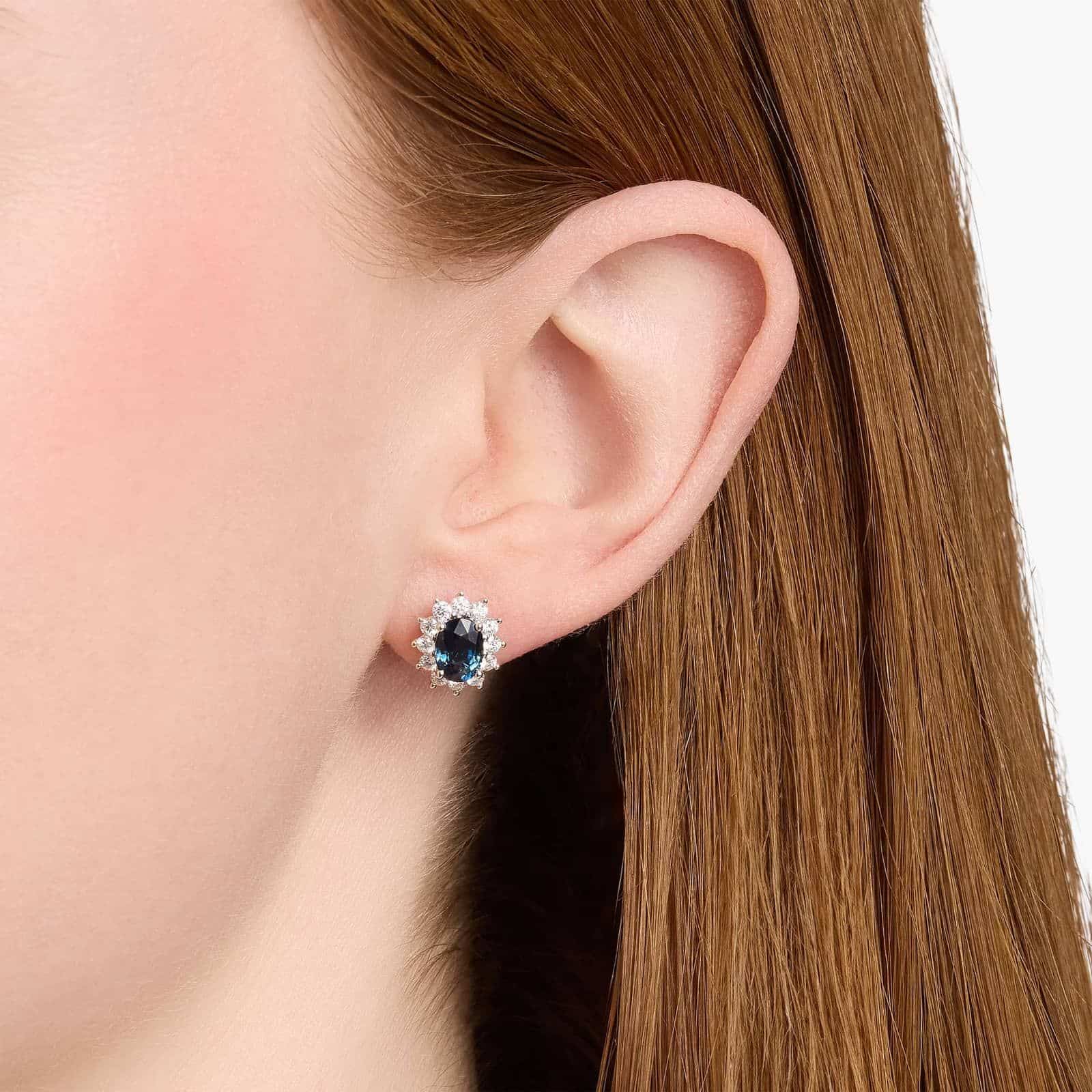 oval-sapphire-diamond-halo-white-gold-and-sapphire-earrings-18k-0-72ctw model view 3 An 18K White Gold White Gold and Sapphire Earrings set featuring two 7x5 mm Oval Blue Sapphires surrounded by a 0.72 CTW Round Diamond Halo, secured with Push Backs.