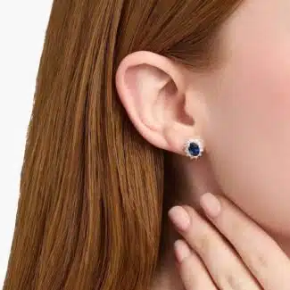 An 18K White Gold White Gold and Sapphire Earrings set featuring two 7x5 mm Oval Blue Sapphires surrounded by a 0.72 CTW Round Diamond Halo, secured with Push Backs.