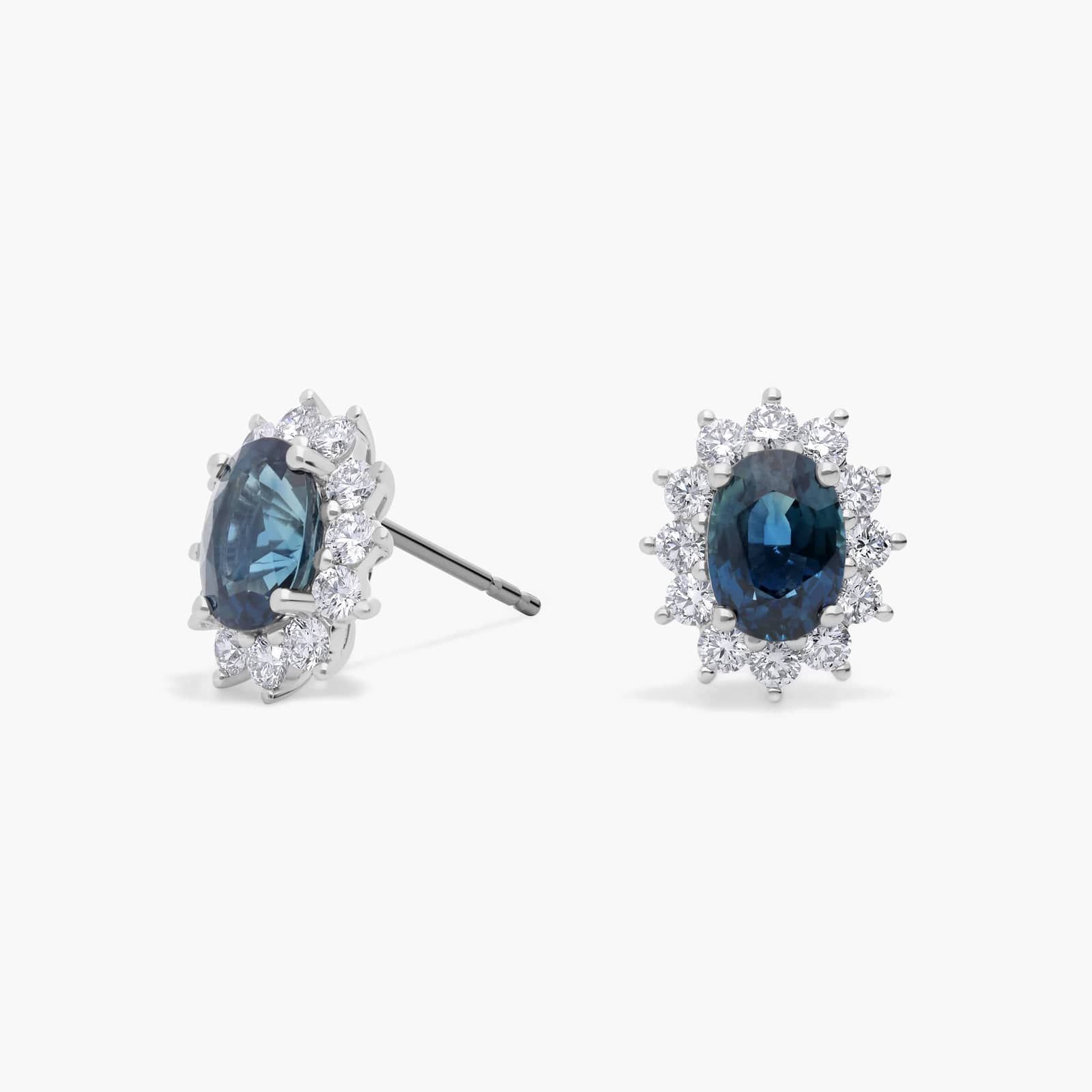 oval-sapphire-diamond-halo-white-gold-and-sapphire-earrings-18k-0-72ctw An 18K White Gold White Gold and Sapphire Earrings set featuring two 7x5 mm Oval Blue Sapphires surrounded by a 0.72 CTW Round Diamond Halo, secured with Push Backs.