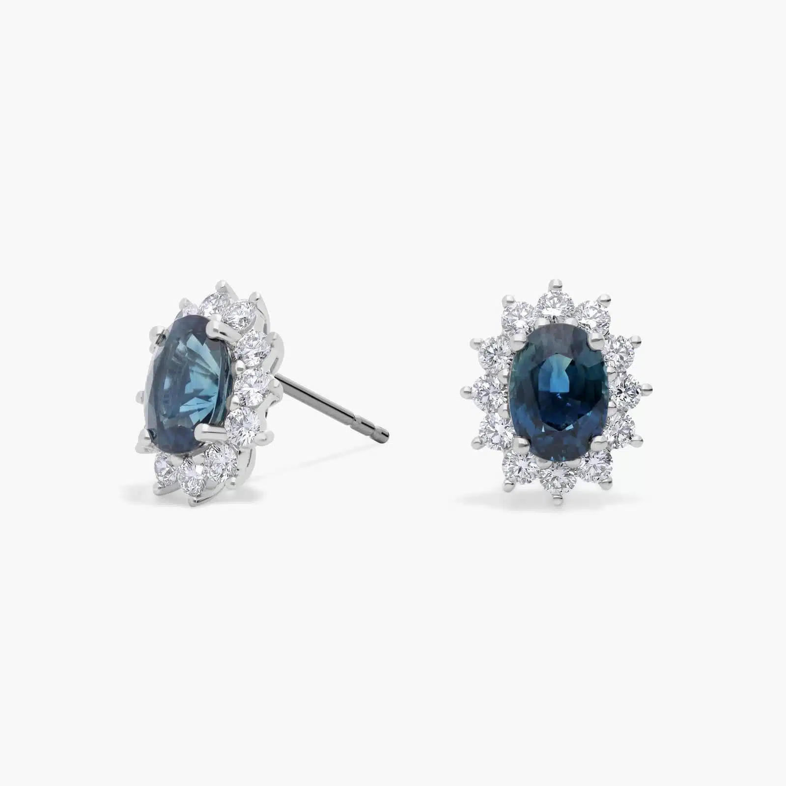 oval-sapphire-diamond-halo-white-gold-and-sapphire-earrings-18k-0-72ctw An 18K White Gold White Gold and Sapphire Earrings set featuring two 7x5 mm Oval Blue Sapphires surrounded by a 0.72 CTW Round Diamond Halo, secured with Push Backs.