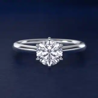 Platinum six prong solitaire engagement rings under $2,500 featuring a 1.5 carat round colorless lab grown diamond on a petite 1.80mm Nouveau band.